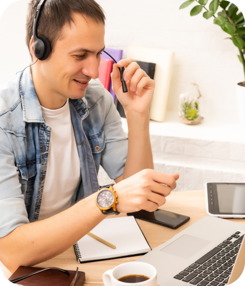 A man working on a laptop is wearing a wired headset and helping customers with their DNS problems.