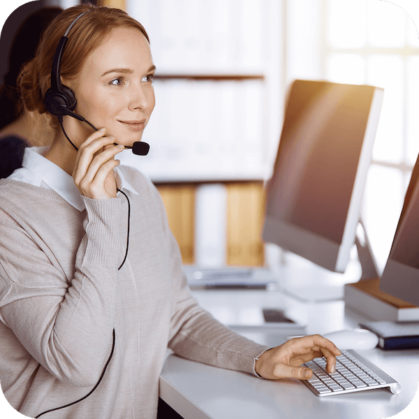 Een vrouw zit voor een computer met een bedrade headset en werkt als klantenservicemedewerker die een gebruiker helpt.