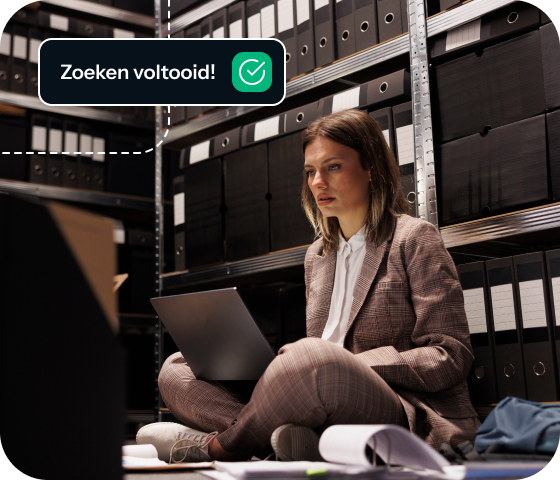 A woman sits cross-legged on the floor using a laptop in a room full of files, depicting the way that Eweka Internet Services offers access to a huge library of information from the Usenet daily feed.