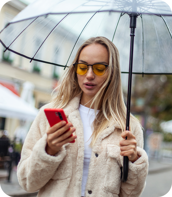 A woman with sunglasses and an umbrella is using her cell phone to connect to a secure VPN on the go