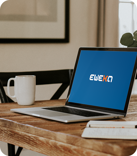 A laptop displaying the Eweka logo is sitting open on a kitchen table beside a white mug.