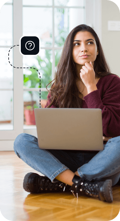 A brunette woman is working on her laptop and giving a thoughtful look to the middle distance.