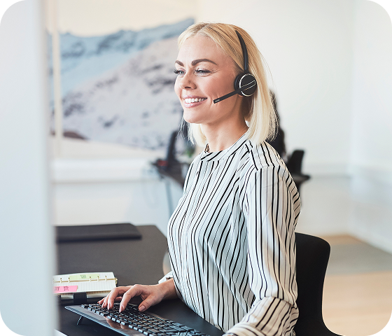 A female technical support agent is sitting in front of a computer keyboard and using a headset to communicate with a customer.