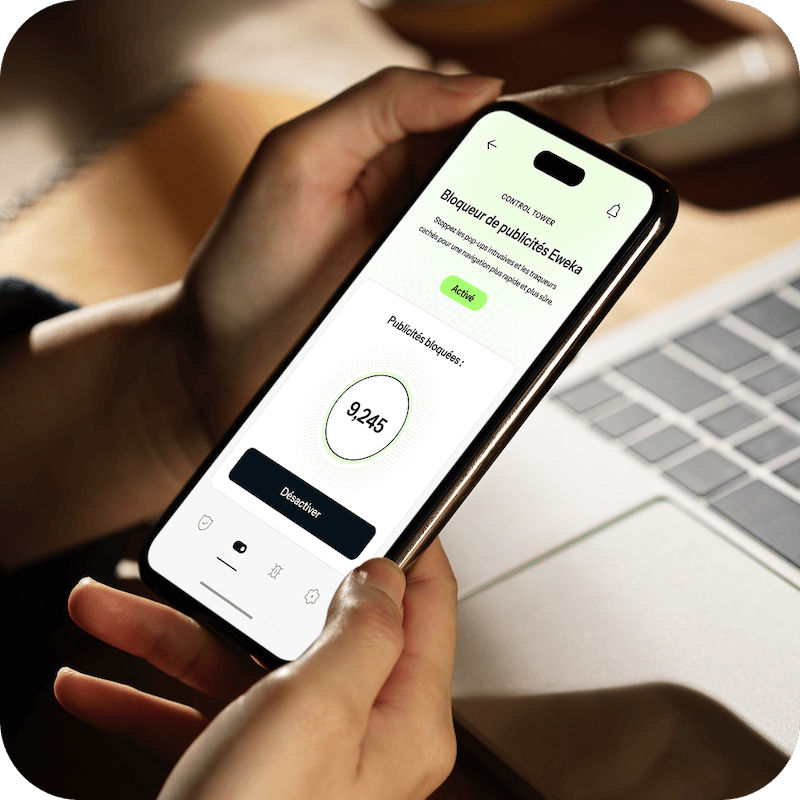 Une paire de mains tient un iPhone ouvert devant un ordinateur portable, où l’iPhone est connecté aux paramètres premium de blocage de publicités d’Eweka pour une protection et une sécurité accrues.
