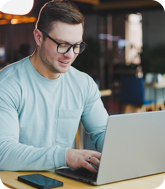 Een man met een bril zit met een laptop in een café en gebruikt Eweka’s VPN voor verbeterde bescherming en beveiliging online en op Usenet.