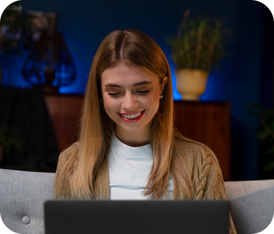 A young woman sits on a couch using a laptop to access Eweka’s Usenet servers and find exactly what she’s searching for across Usenet.