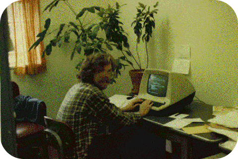 Jim Ellis travaillant sur un ordinateur de bureau à la fin des années 1970. Il porte une moustache imposante et regarde la caméra.