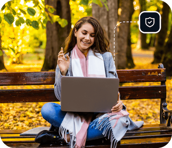 Een vrouw zit buiten op een parkbank met een laptop om te videochatten op haar apparaat dat is verbonden met Eweka’s VPN en de premium dreigingsbeschermingsinstellingen voor geavanceerde beveiliging.