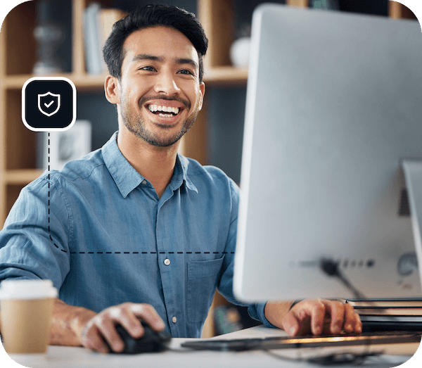 A man with short, black hair is working at his desktop with a big smile on his face.